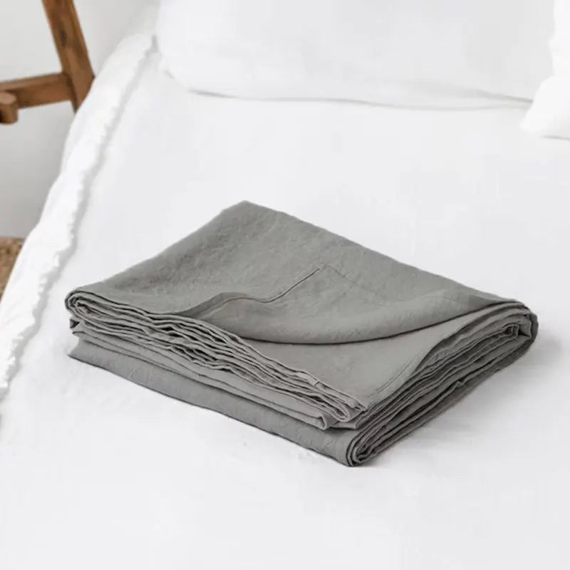 A stack of soft gray pure French linen bed sheets folded neatly on a white bed.