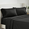 Black striped bedding set with a white upholstered headboard and a vase of white flowers.