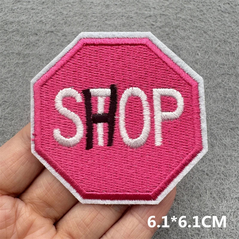 Pink hexagonal embroidered patch with the word SHOP in white and black thread