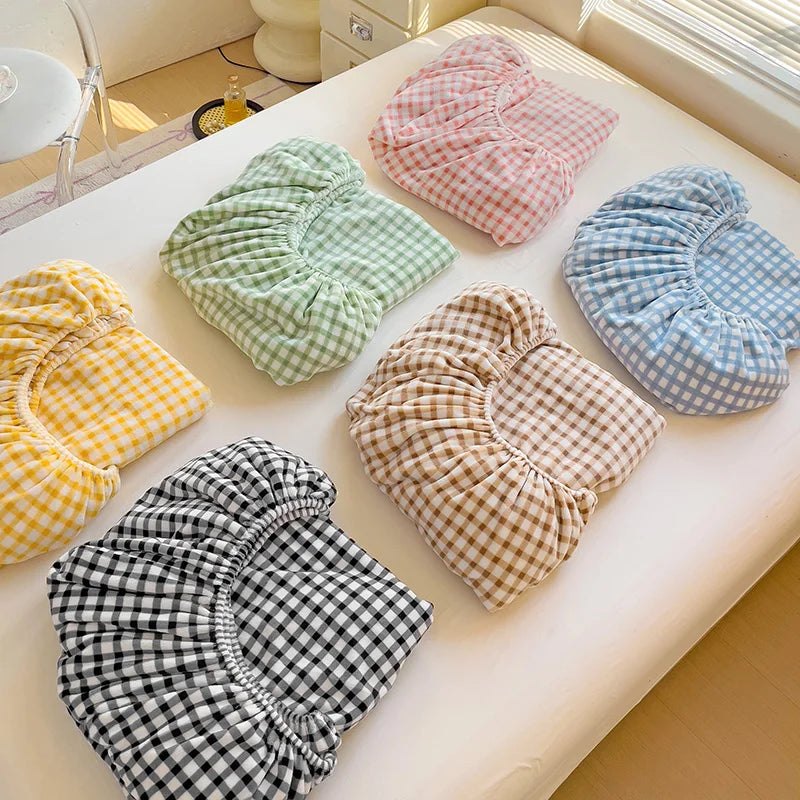 A collection of plaid flannel fitted sheets in various colors including pink, green, blue, and yellow stacked on a white tabl