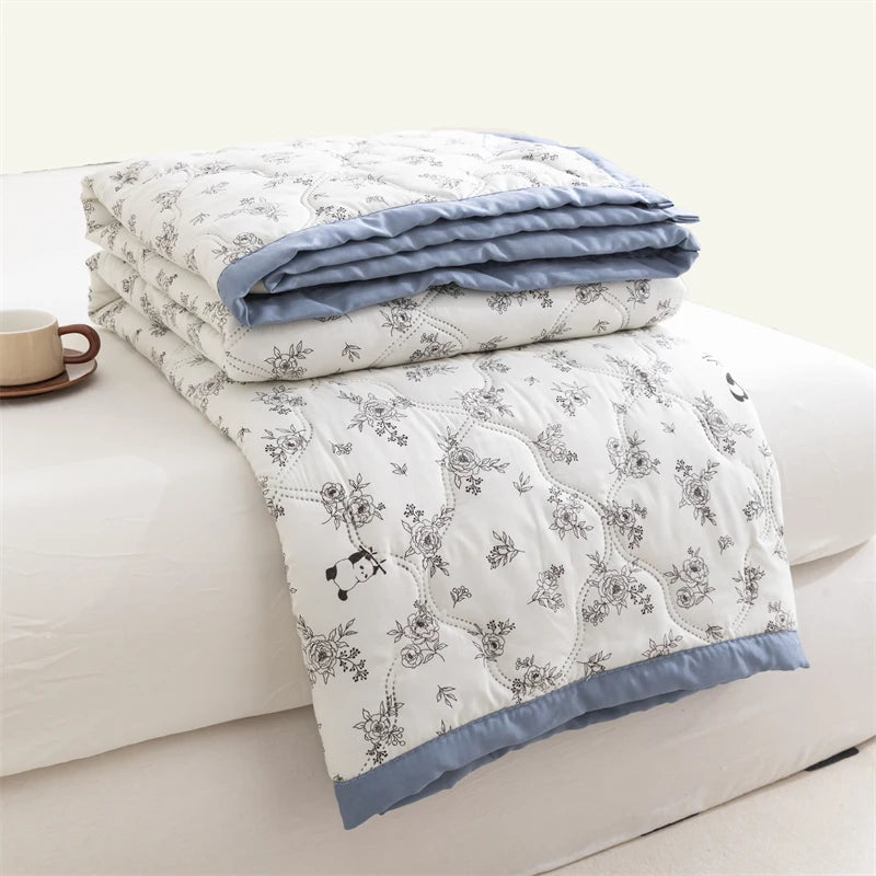 A stack of light blue and white floral patterned duvet covers folded on a white bed.