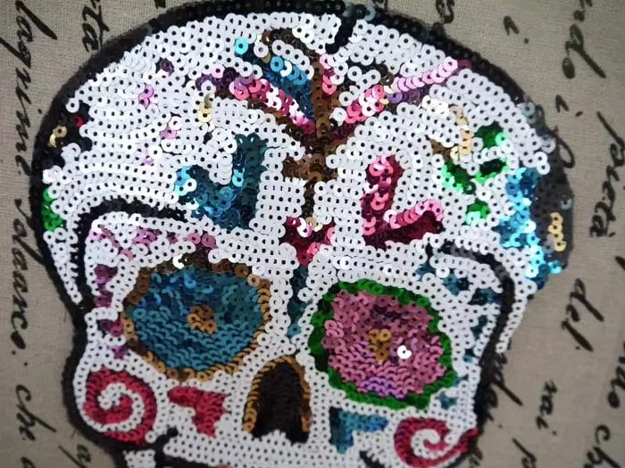 A detailed embroidered patch of a skull made from iridescent sequins and colorful threads.