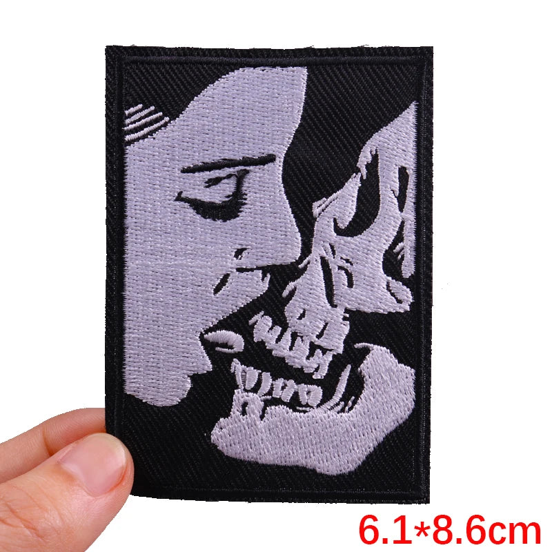 Black embroidered patch featuring a stylized human face and skull in light gray thread