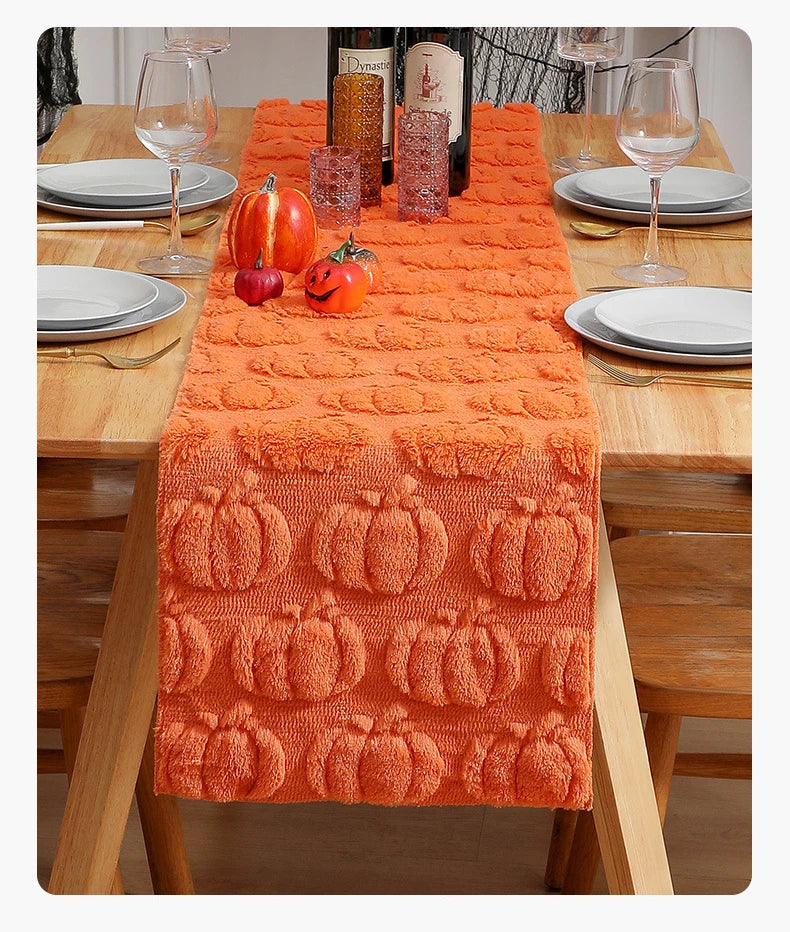 An orange festive Halloween table runner displayed on a wooden table with pumpkins and glassware.