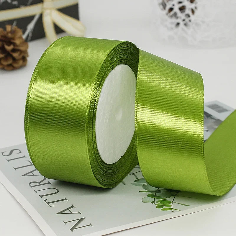 A roll of smooth, satin green ribbon with a white center core is shown on a piece of paper.