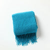 A bright turquoise knitted tassel throw blanket with a ribbed texture and long fringe.