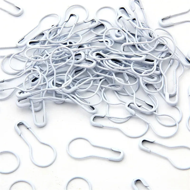A pile of silver safety bulb pins for knitting and sewing scattered on a white surface.