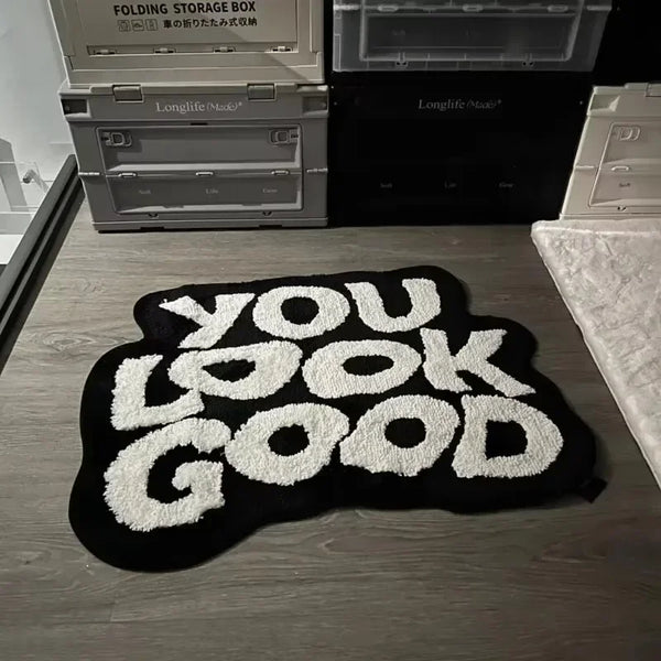 A black foot mat with white text that reads YOU LOOK GOOD is placed in front of a stack of electronic boxes.