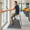 A man sits on an anti-fatigue PVC kitchen mat at a modern desk working on a laptop.