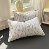 A white duvet cover set with patterned pillowcases rests on a dark surface next to a yellow alarm clock.
