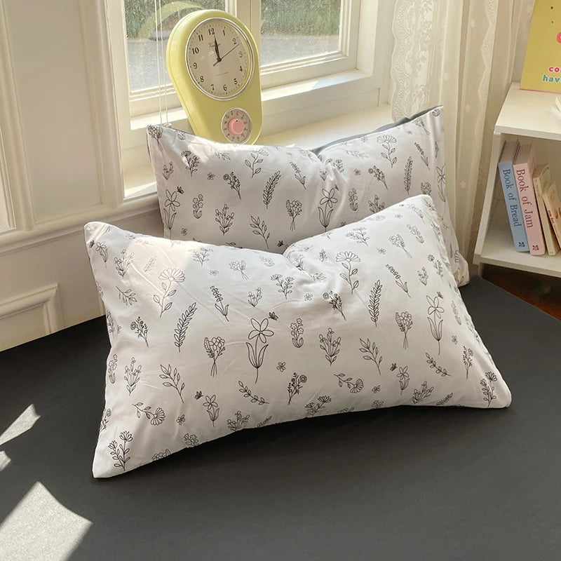 A white duvet cover set with patterned pillowcases rests on a dark surface next to a yellow alarm clock.