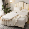 A set of three white embroidered cotton bedspreads and pillowcases displayed on a bed with gold accents.