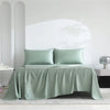 A luxury organic bamboo bed sheet set in sage green color draped over a bed.