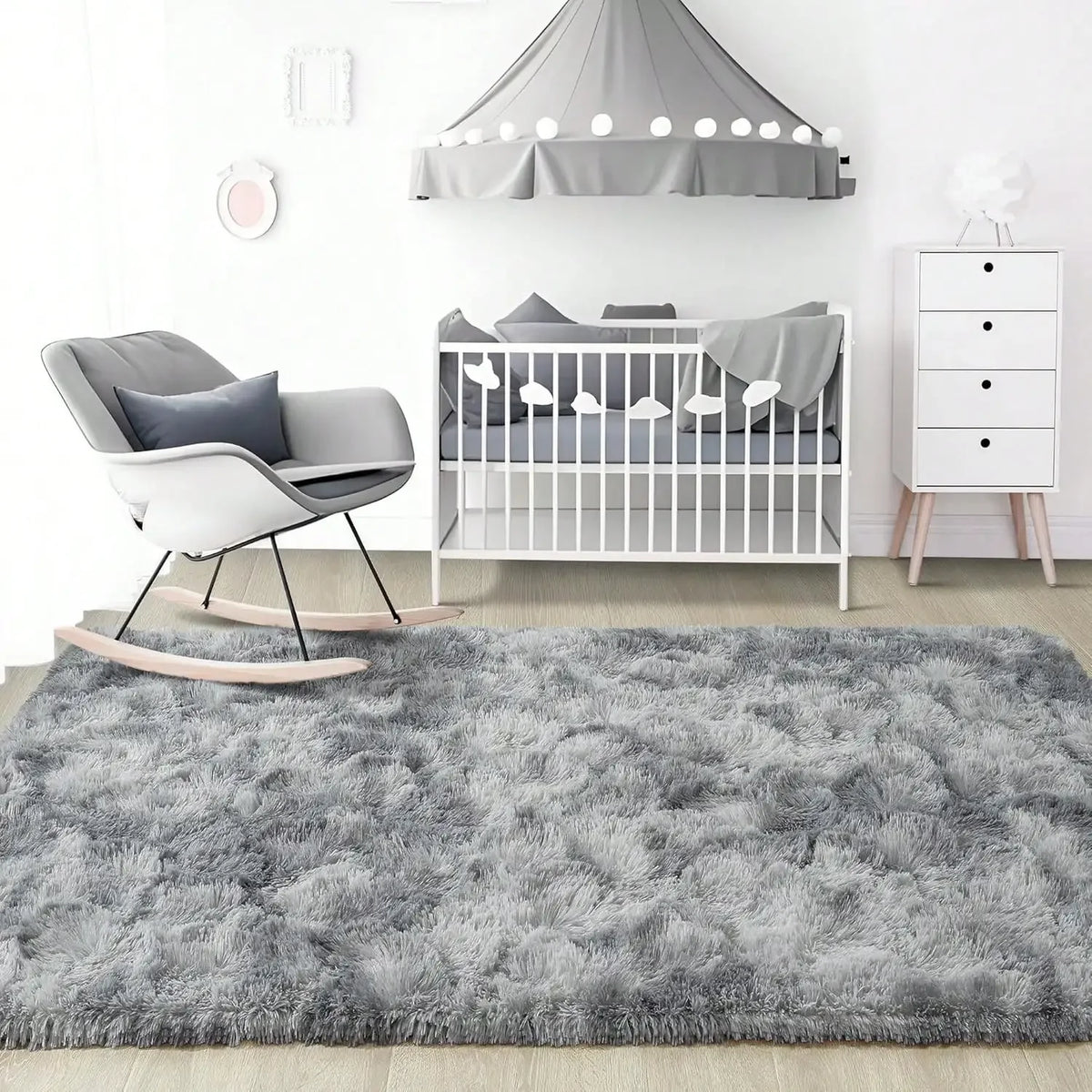 A plush gray long-pile area rug placed in front of a white crib and a gray fabric shade.