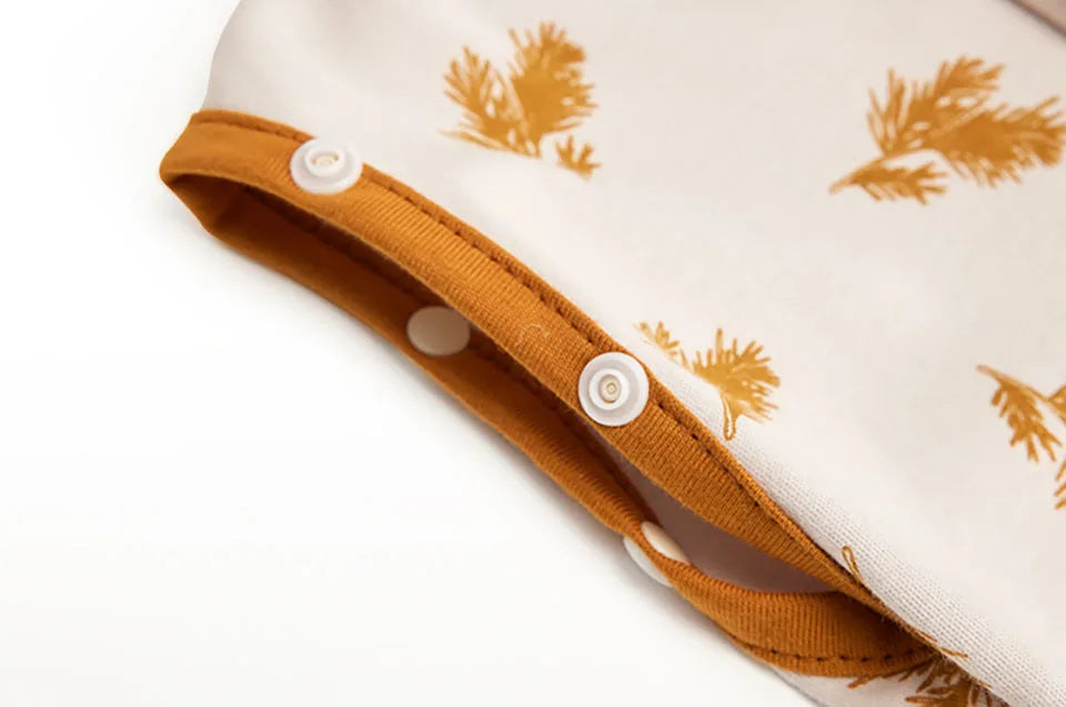 A close-up of a beige soft cotton baby sleeping bag or swaddle with a mustard yellow print and wooden buttons.
