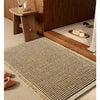 A woven waffle bath mat in beige rests on a wooden floor next to a wooden stand.