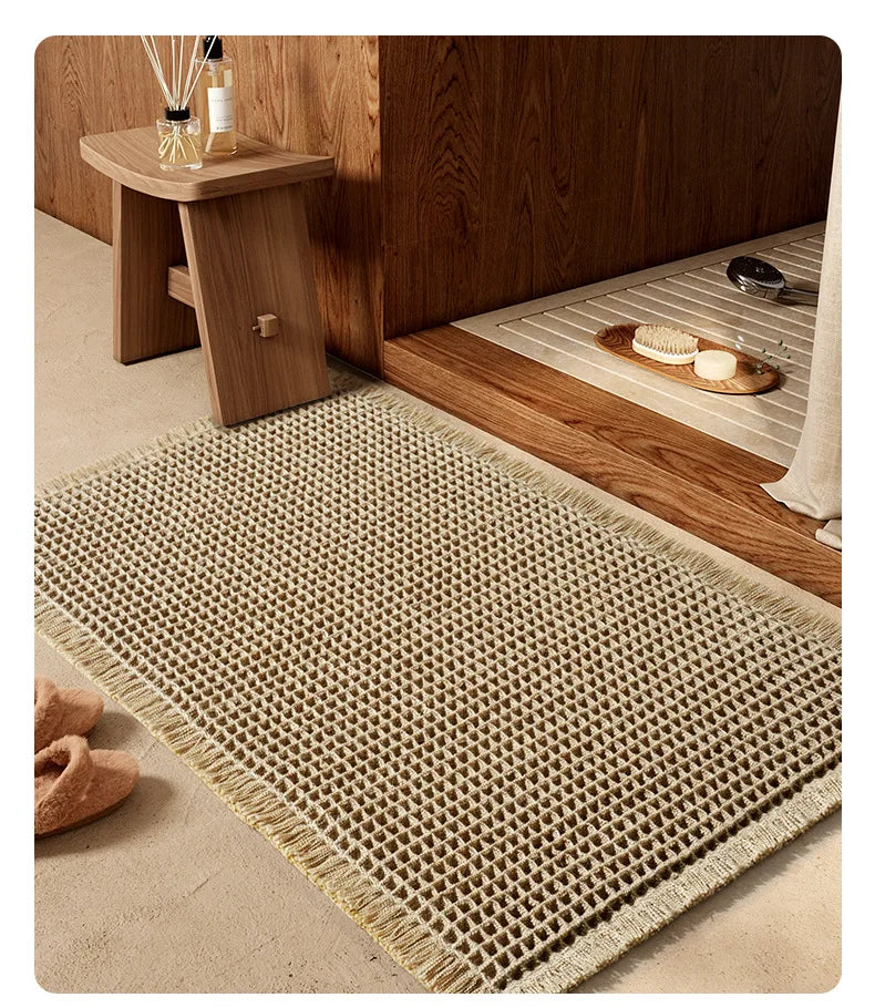 A woven waffle bath mat in beige rests on a wooden floor next to a wooden stand.