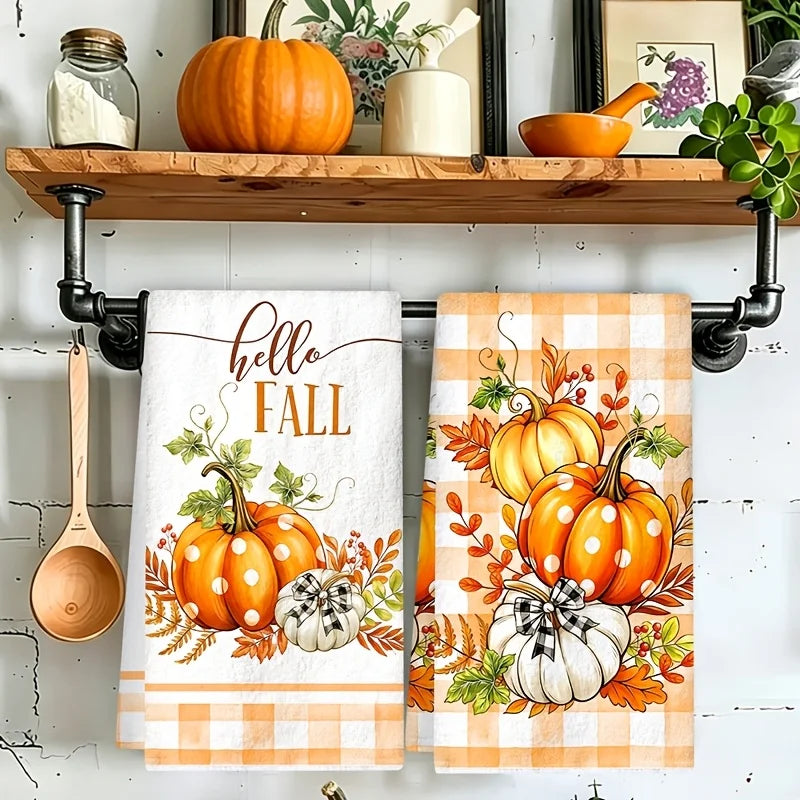 A set of two kitchen towels featuring an orange and white plaid design with pumpkins and foliage.