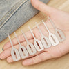 A hand holds a set of stainless steel needle threaders for hand sewing and embroidery.