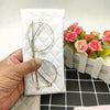 A hand holds a white quilted pouch containing a pair of gold-rimmed eyeglasses and a cleaning cloth.