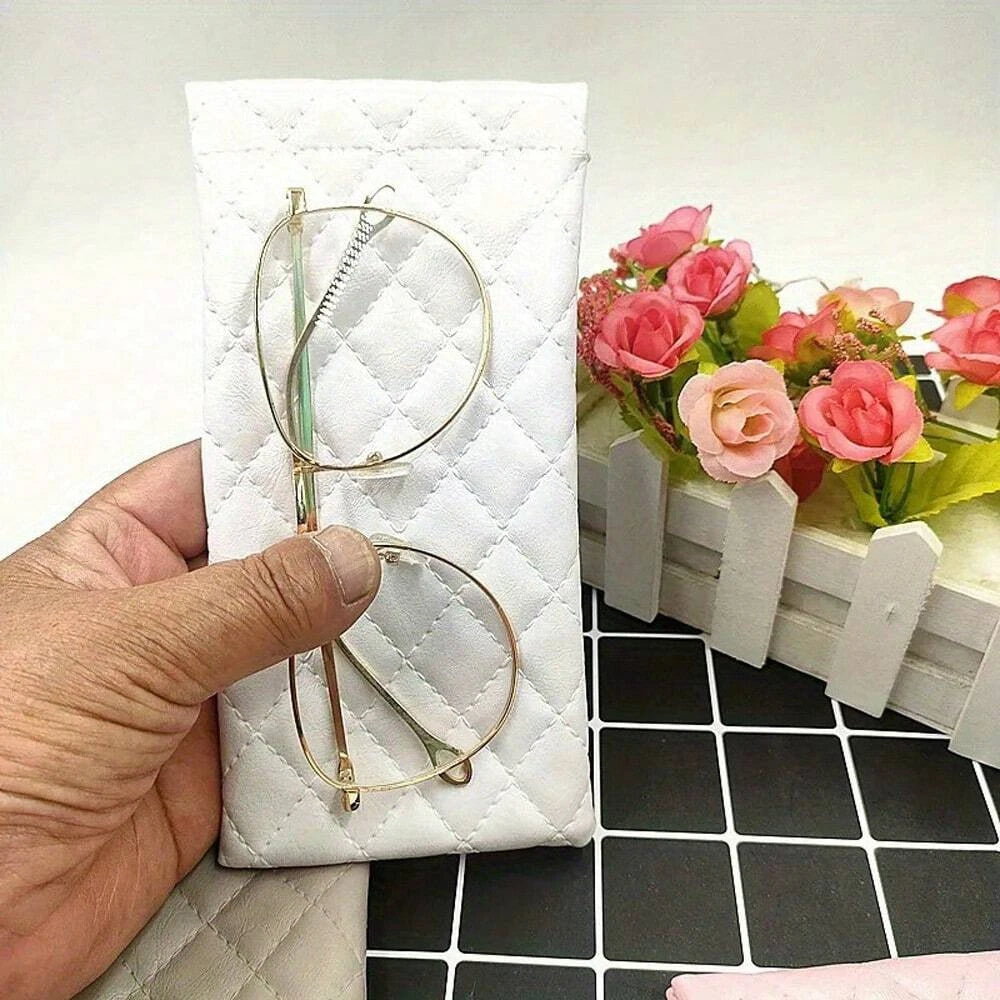 A hand holds a white quilted pouch containing a pair of gold-rimmed eyeglasses and a cleaning cloth.