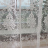 Sheer white embroidered curtains with floral designs covering a glass window.