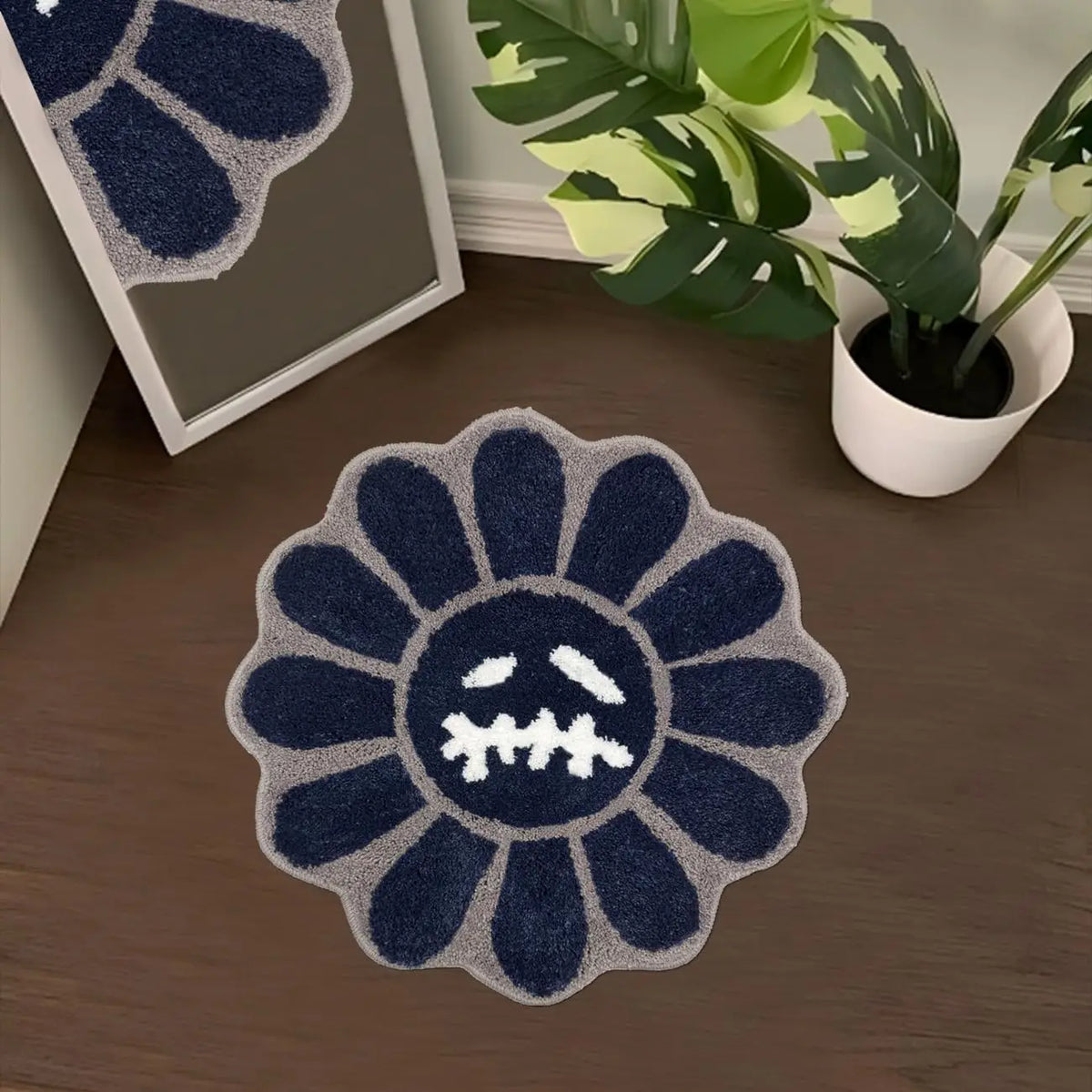 A dark blue and gray textured mat shaped like a sunflower with a distressed face on a wooden floor.