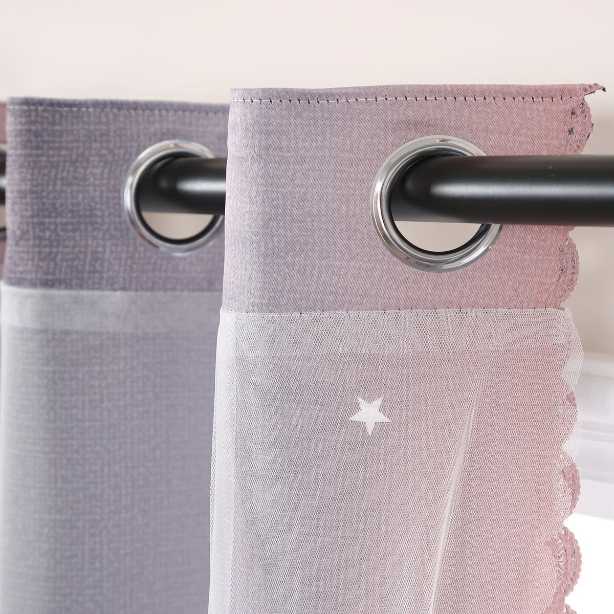 A close-up of grey-pink gradient star perforated curtains hanging on a black rod.