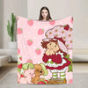 A pink strawberry shortcake plush throw blanket featuring a character and fruit patterns.