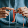 Hands are using a thin tool to manipulate orange crochet tension rings on a string.