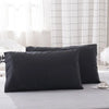 A set of two black soft polyester pillow covers resting on a light gray bed.