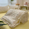 A rolled white quilt blanket with a subtle floral print rests on a yellow surface.