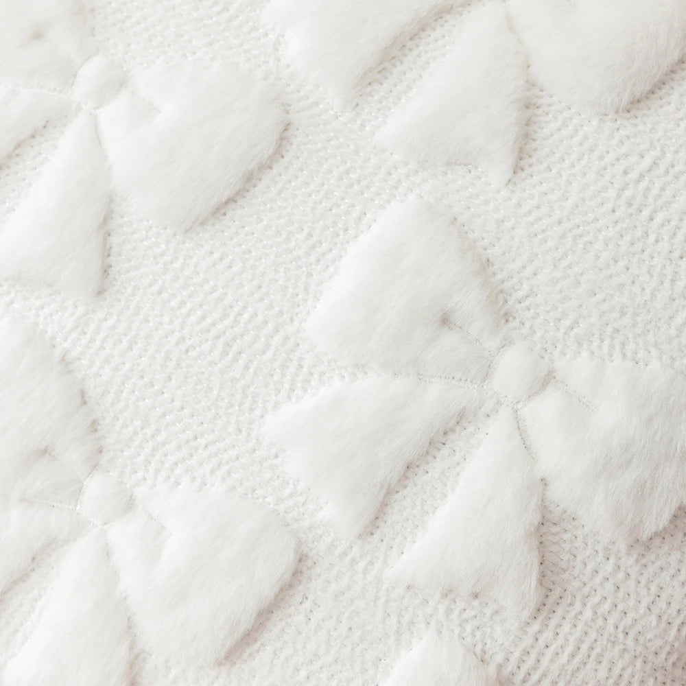 A close-up view of white faux fur pillow covers with a subtle diamond pattern on a textured fabric.