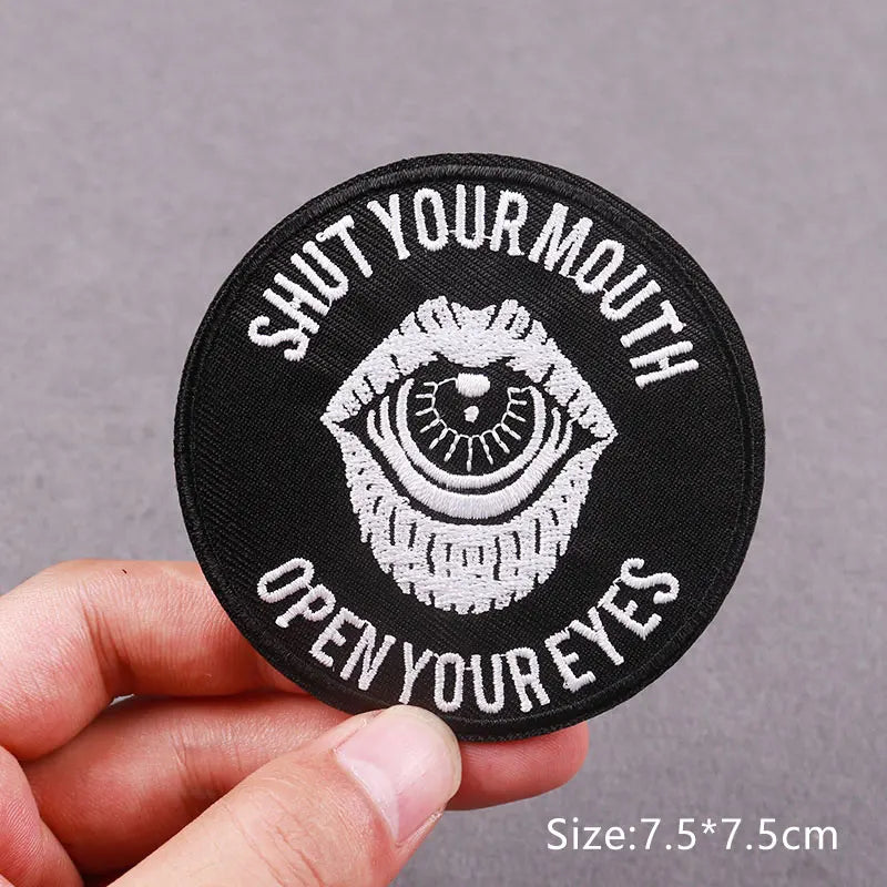 Black embroidered patch with white text Shut Your Mouth Open Your Eyes