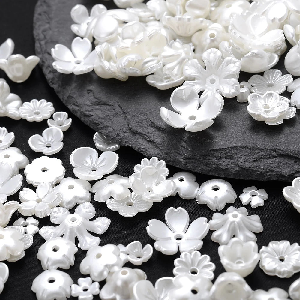 A pile of white imitation pearl flower spacer beads scattered on a dark surface.