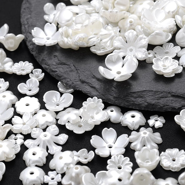 A pile of white imitation pearl flower spacer beads scattered on a dark surface.