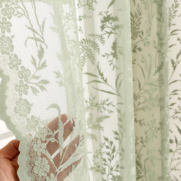 Close-up of sheer lace floral window curtains in pale green and white, showing the delicate pattern and texture.