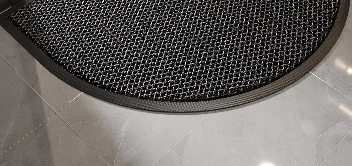 A close-up view of a black half-round non-slip PVC door mat with a diamond pattern placed on a light gray tiled floor.
