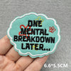 A teal embroidered patch with the text ONE MENTAL BREAKDOWN LATER embroidered in red and yellow thread.