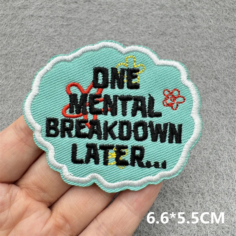 A teal embroidered patch with the text ONE MENTAL BREAKDOWN LATER embroidered in red and yellow thread.