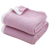 A folded light pink muslin throw blanket with white trim and stitching.
