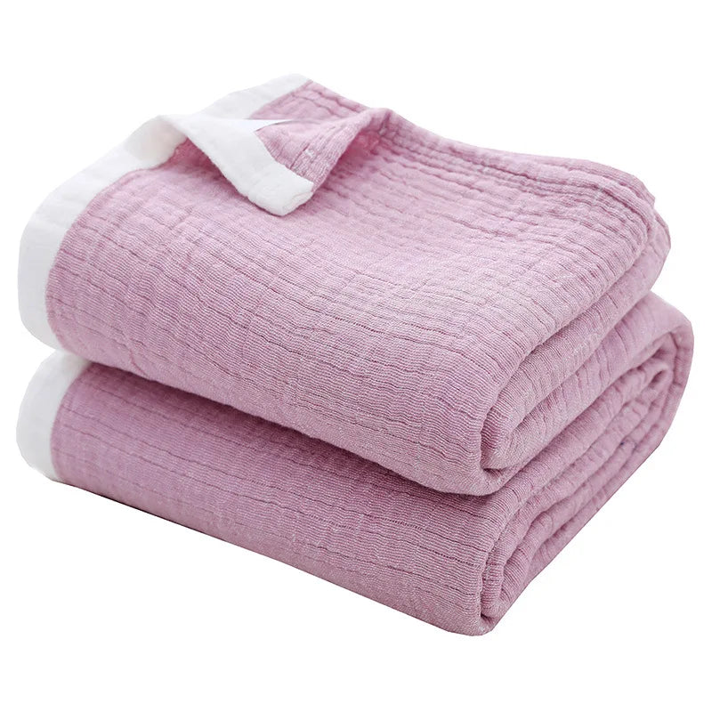 A folded light pink muslin throw blanket with white trim and stitching.