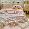 A pink quilt blanket with a summer floral print is displayed on a bed, next to a stuffed bear and various household items.