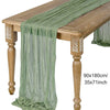 A light green semi-sheer gauze fabric draped over a wooden table, used as a table runner for elegant decor.