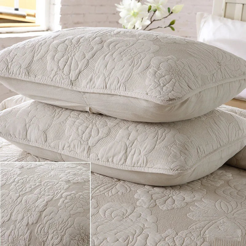 A set of light gray embroidered cotton quilted pillow covers stacked on a white surface.