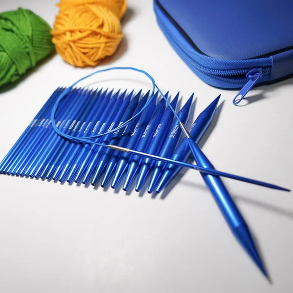 A set of blue interchangeable circular knitting needles lying on a white surface next to yarn and a blue pouch.