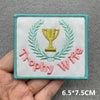 A square embroidered patch featuring a golden trophy surrounded by laurel leaves and pink embroidered text