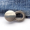 Silver spring-loaded button attached to a denim fabric background.