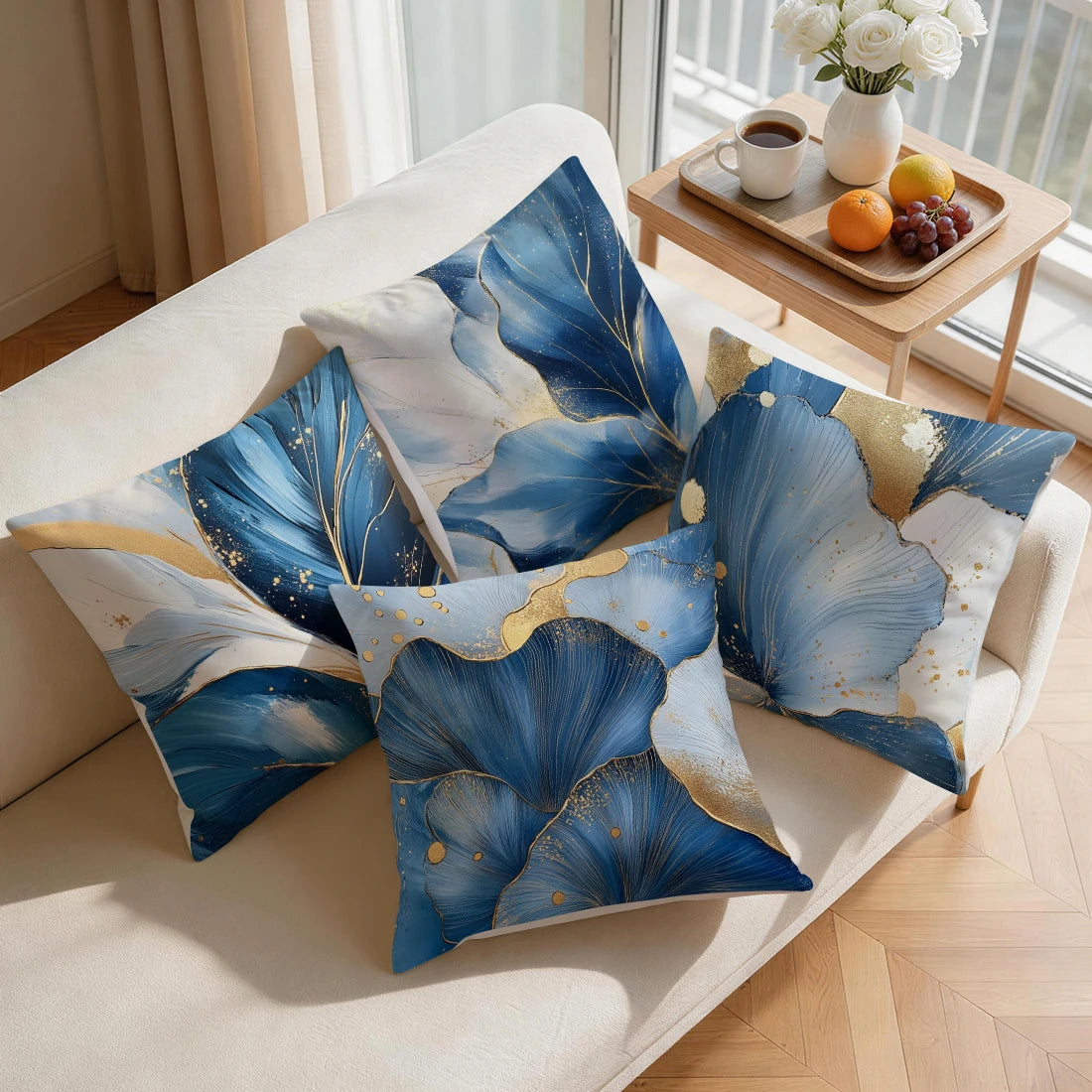 A set of abstract leaf cushion pillow covers in shades of blue and gold displayed on a light-colored sofa.