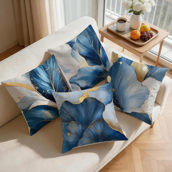 A set of abstract leaf cushion pillow covers in shades of blue and gold displayed on a light-colored sofa.